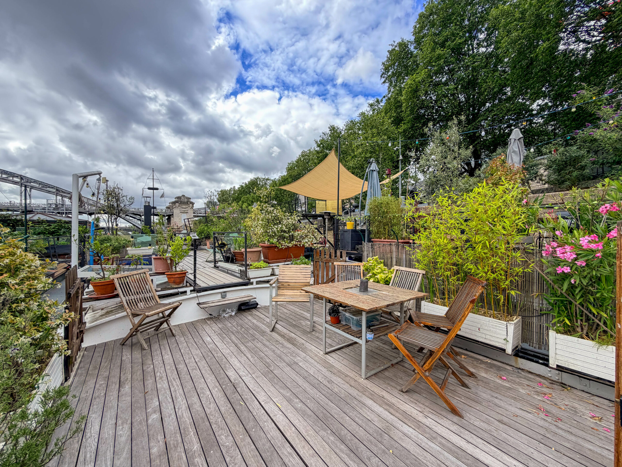 Terrasse en bois aménagée et végétalisée sur une péniche habitable navigante à vendre à Paris 13e, avec vue sur la Seine.